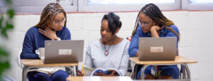Three young women sitting at desks with laptops.