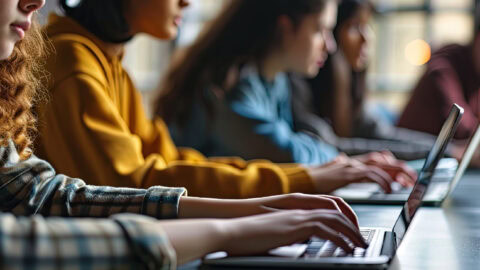 Several people sitting at a table with laptops, typing on keyboards.