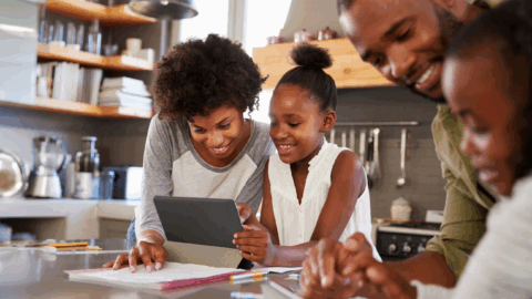 A family is looking at a tablet in the kitchen.