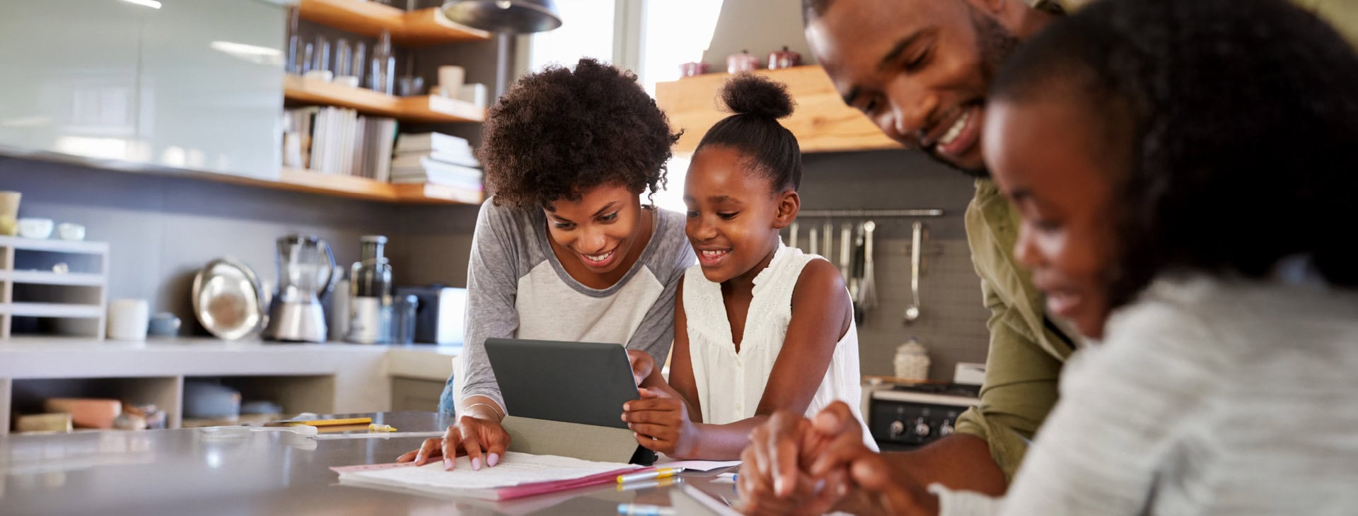 A family is looking at a tablet in the kitchen.