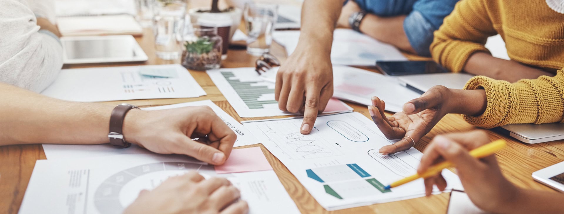 A desk covered in papers with people pointing at key information on the papers.