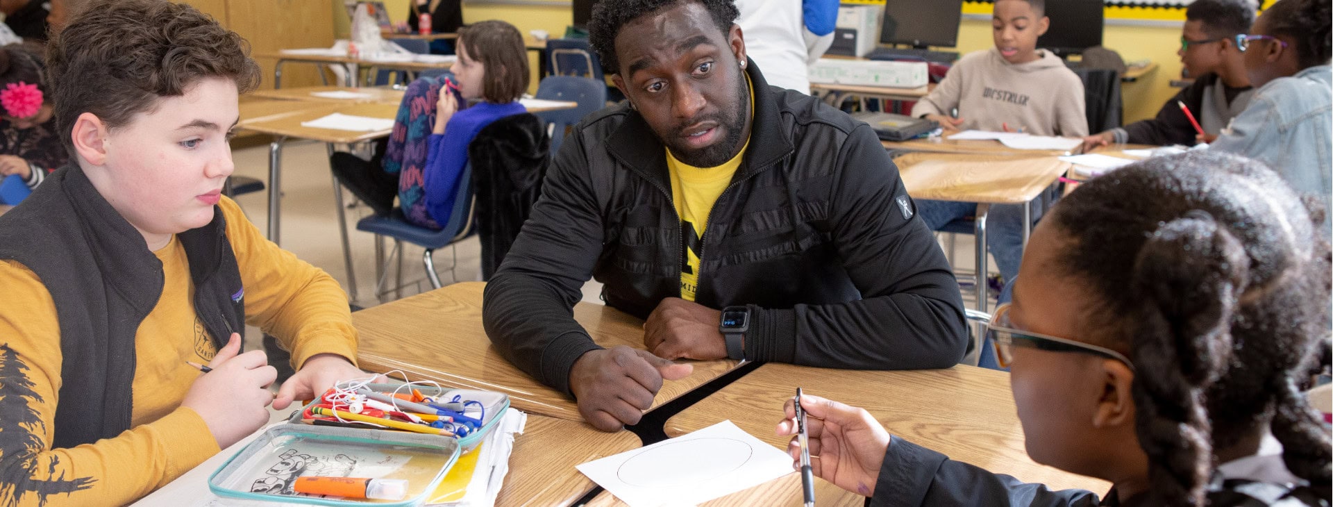A teacher works with two students at a table.