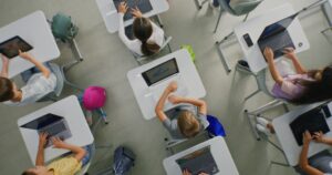 Image shows students sitting at desks, working on laptop computers.
