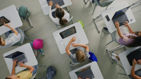 Image shows students sitting at desks, working on laptop computers.
