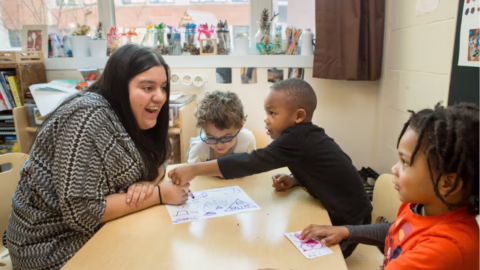 Teacher works with three young children at a table in a classroom.