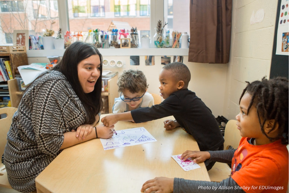 Teacher works with three young children at a table in a classroom.
