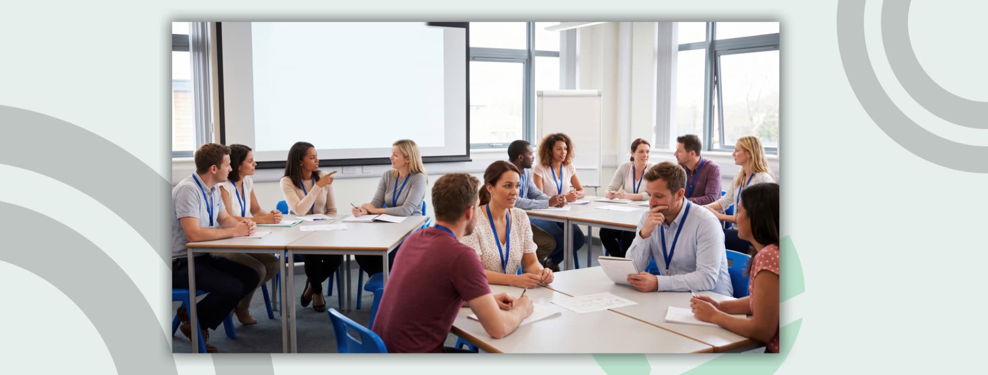 Teachers having a discussion while seated at three tables in a classroom.